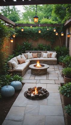 an outdoor fire pit surrounded by greenery and potted plants with lights hanging from the ceiling