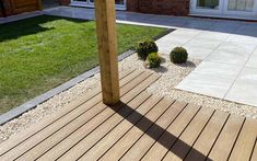 a wooden deck in front of a house with grass and bushes on the ground next to it