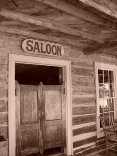 an old wooden building with two doors and a rocking chair on the front porch in black and white