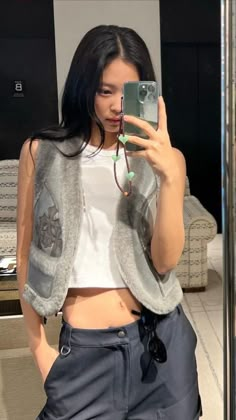 a woman taking a selfie in front of a mirror wearing grey pants and a white crop top