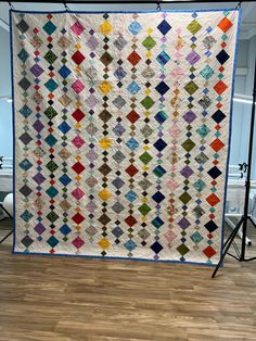 a quilt is displayed on a tripod in the middle of a room with wooden floors