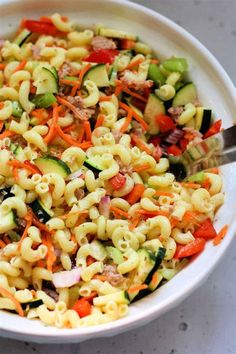 a white bowl filled with pasta salad on top of a marble counter next to a silver spoon