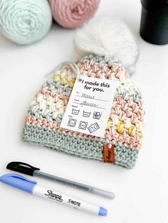 a crocheted hat with a note on it next to two balls of yarn