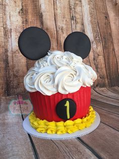 a mickey mouse cupcake with white frosting and ears on top, sitting on a wooden table