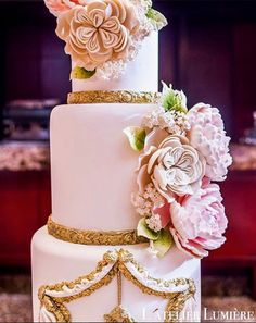 a three tiered wedding cake with pink flowers on the top and gold trimmings