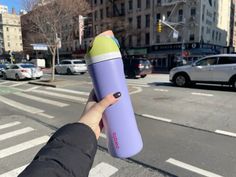 a person holding up a purple and green water bottle in the middle of a street