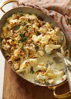 a pan filled with cauliflower on top of a wooden cutting board next to a fork