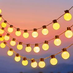 a string of light bulbs hanging from the side of a building at dusk with mountains in the background