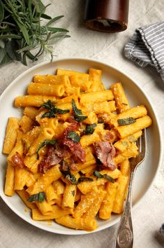 a white plate topped with pasta covered in bacon and spinach next to a bottle of wine