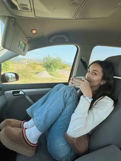 a woman sitting in the back seat of a car talking on a cell phone and drinking from a cup