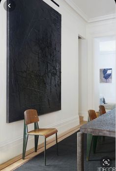 a large black painting hanging on the wall in a room with two chairs and a table