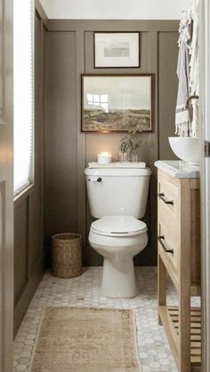 a white toilet sitting inside of a bathroom next to a wooden cabinet and sink under a mirror