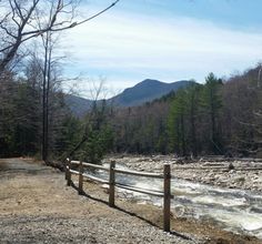 a wooden fence next to a river with mountains in the background