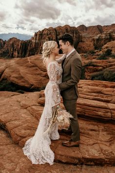 a bride and groom standing on top of a rock formation in the desert with mountains behind them