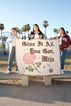 three people standing next to a sign that says give it all don't miss