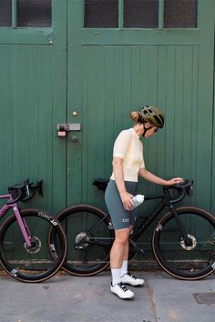 a woman standing next to two bikes on the side of a building with green doors