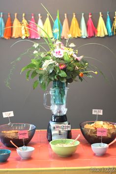 a table topped with bowls of food and a blender filled with flowers on top of it