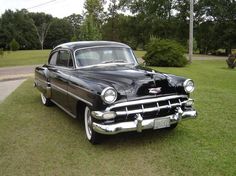 an old black car is parked in the grass