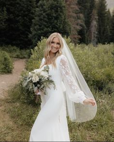 a woman in a white wedding dress holding a bouquet and wearing a long veil over her head