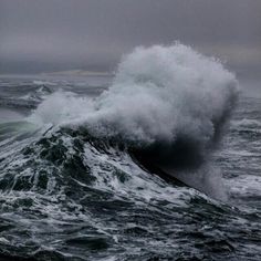 a large wave crashing into the ocean on a cloudy day