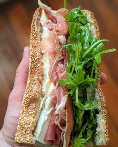 a sandwich with meat, lettuce and cheese on it in someone's hand