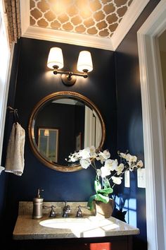 a bathroom with blue walls and white flowers on the counter top, along with a gold framed mirror