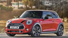 a red mini cooper hatchback parked on the side of a road with palm trees in the background