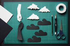 paper clouds and scissors on a cutting board with tape, scissors, and other crafting supplies