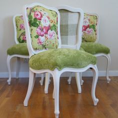 two white chairs with green floral cushions on them sitting in a room next to a wall