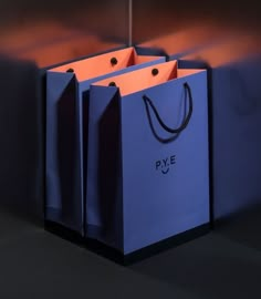 two blue shopping bags sitting on top of each other in front of a black wall