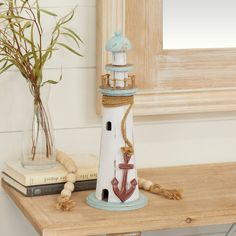 a white lighthouse with an anchor painted on the side and rope around it sitting on a wooden table next to a potted plant