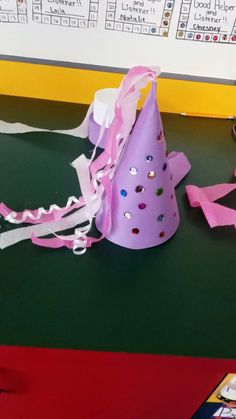 a purple party hat sitting on top of a green table next to pink ribbons and scissors