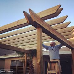 a man standing on top of a ladder next to a wooden pergolated roof