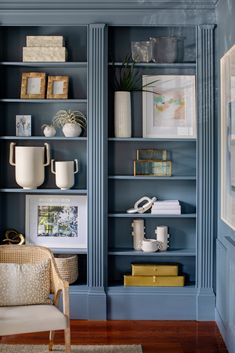 a blue bookcase filled with lots of books next to a chair and vases