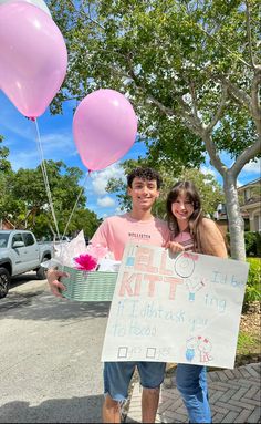 a man and woman holding up pink balloons in front of a sign that says help kit