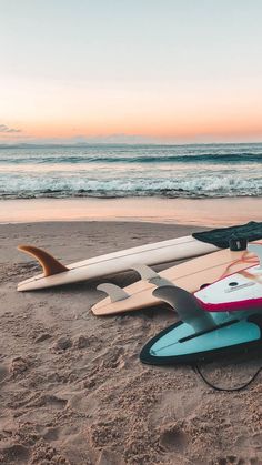 two surfboards are laying on the sand near the ocean at sunset, with one upside down