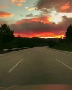 the sun is setting on an empty road with trees and hills in the back ground