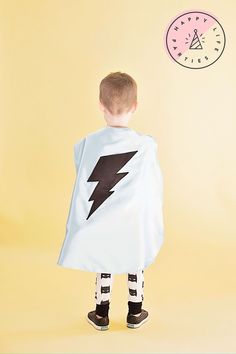 a little boy wearing a cape with a lightning bolt on it's back, standing in front of a yellow background