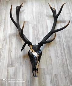 a deer's head with gold and black paint on it sitting on a wooden floor