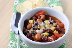 a white bowl filled with beans, corn and tortilla chips on top of a green napkin