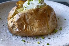 a baked potato with sour cream and chives on it sitting on a white plate