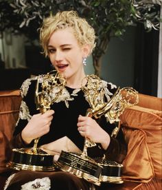 a woman sitting on top of a couch holding two golden trophy cups in her hands