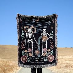 a person standing on a road holding up a blanket with two skeletons in the background