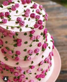 a three tiered cake with pink frosting and purple flowers on the top layer