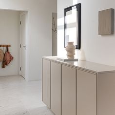 a white room with a mirror, vase and other items on the counter in front of it