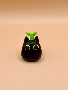 a small black cat figurine with a green leaf on its head and eyes