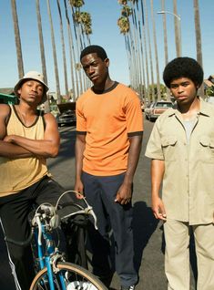 three young men standing next to each other with their bikes in front of palm trees