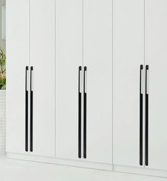 a white cabinet with black handles next to a potted plant