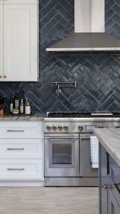 a kitchen with white cabinets and stainless steel stove top oven, range hood, and marble counter tops