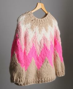 a sweater hanging on a wooden hanger with pink and beige colors in the background